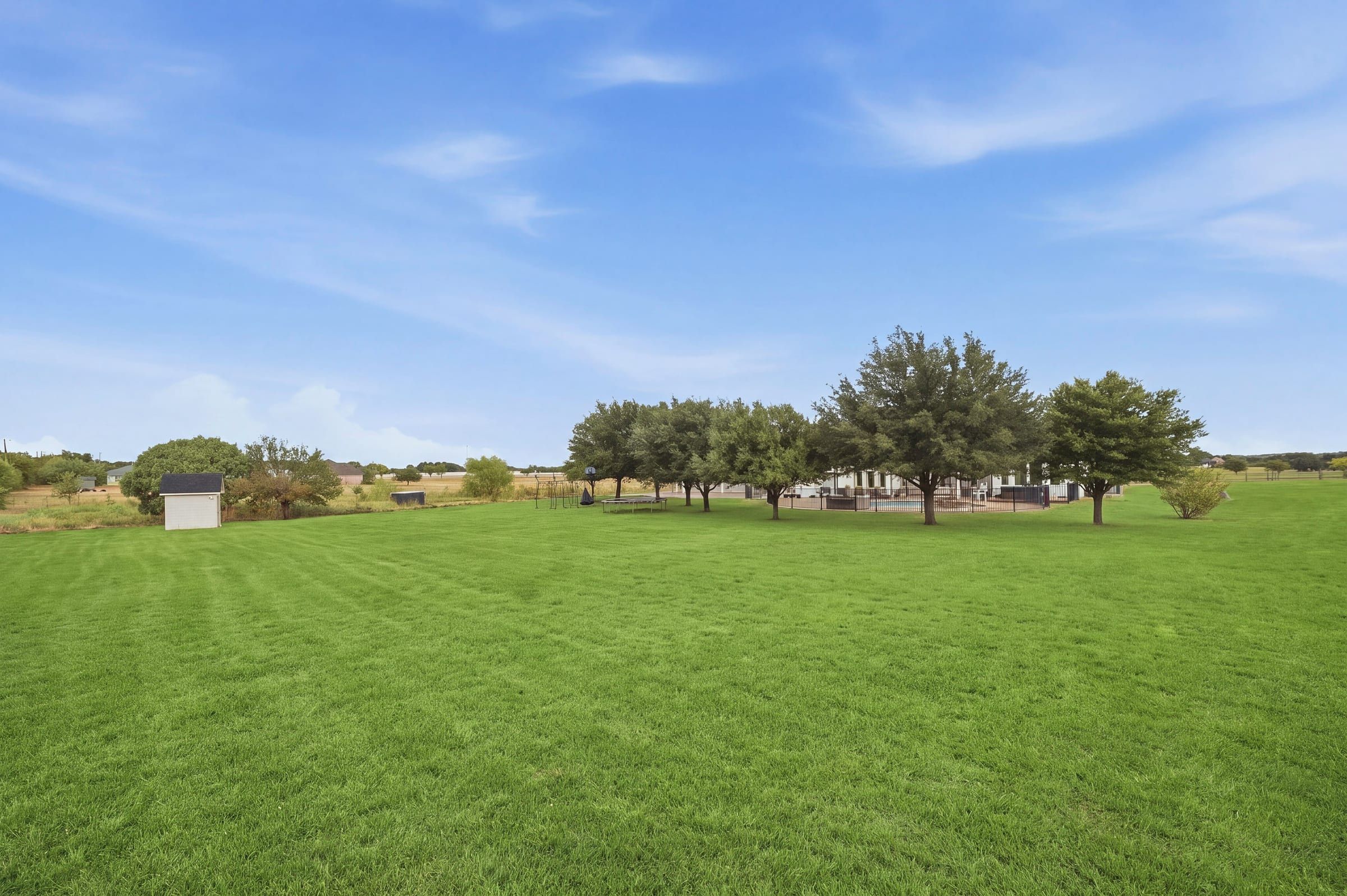 Back acreage with a storage shed and trees around the pool area