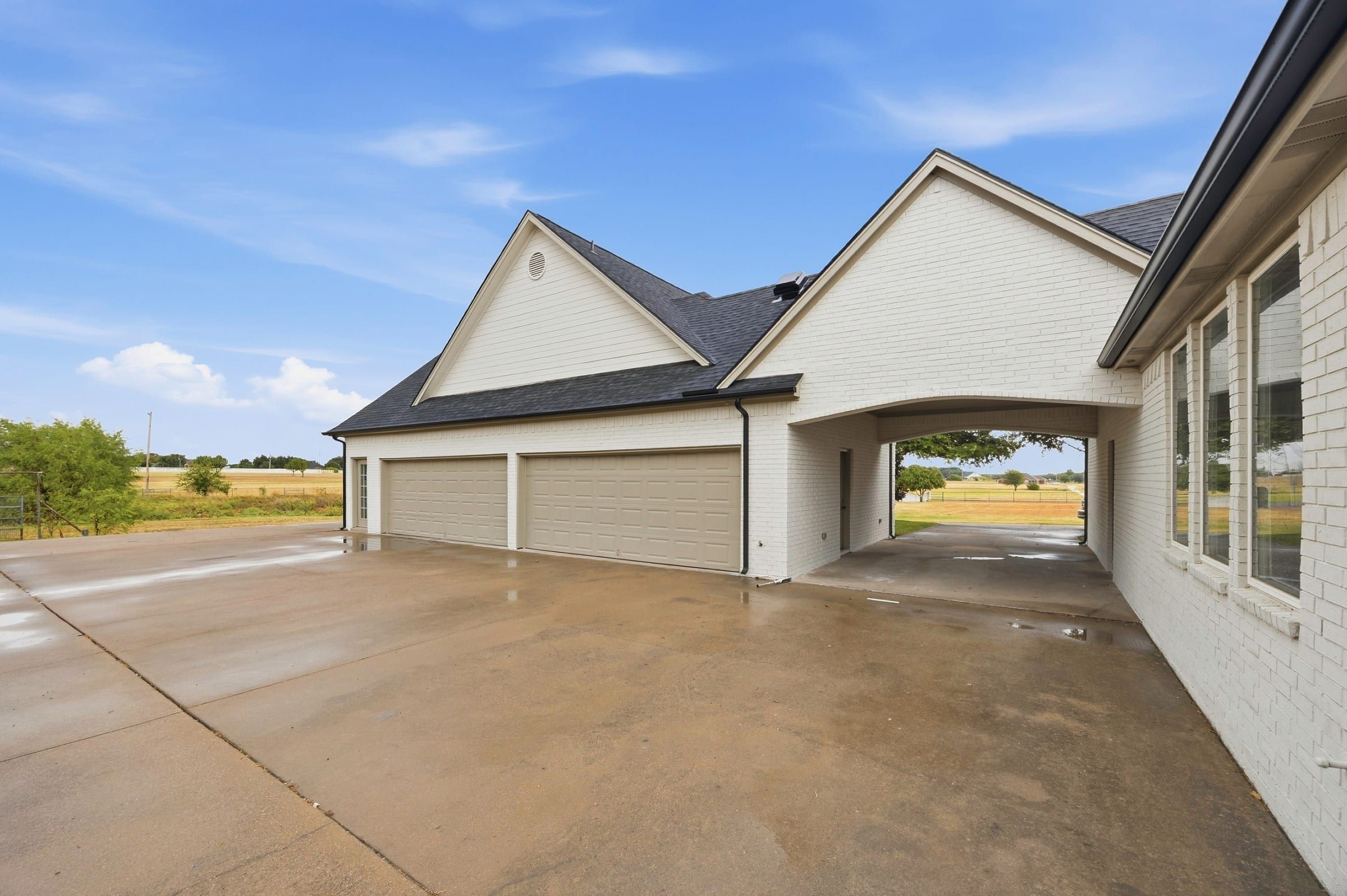 Detached garage with two double doors, connected to the house by a carport, with wide concrete parking